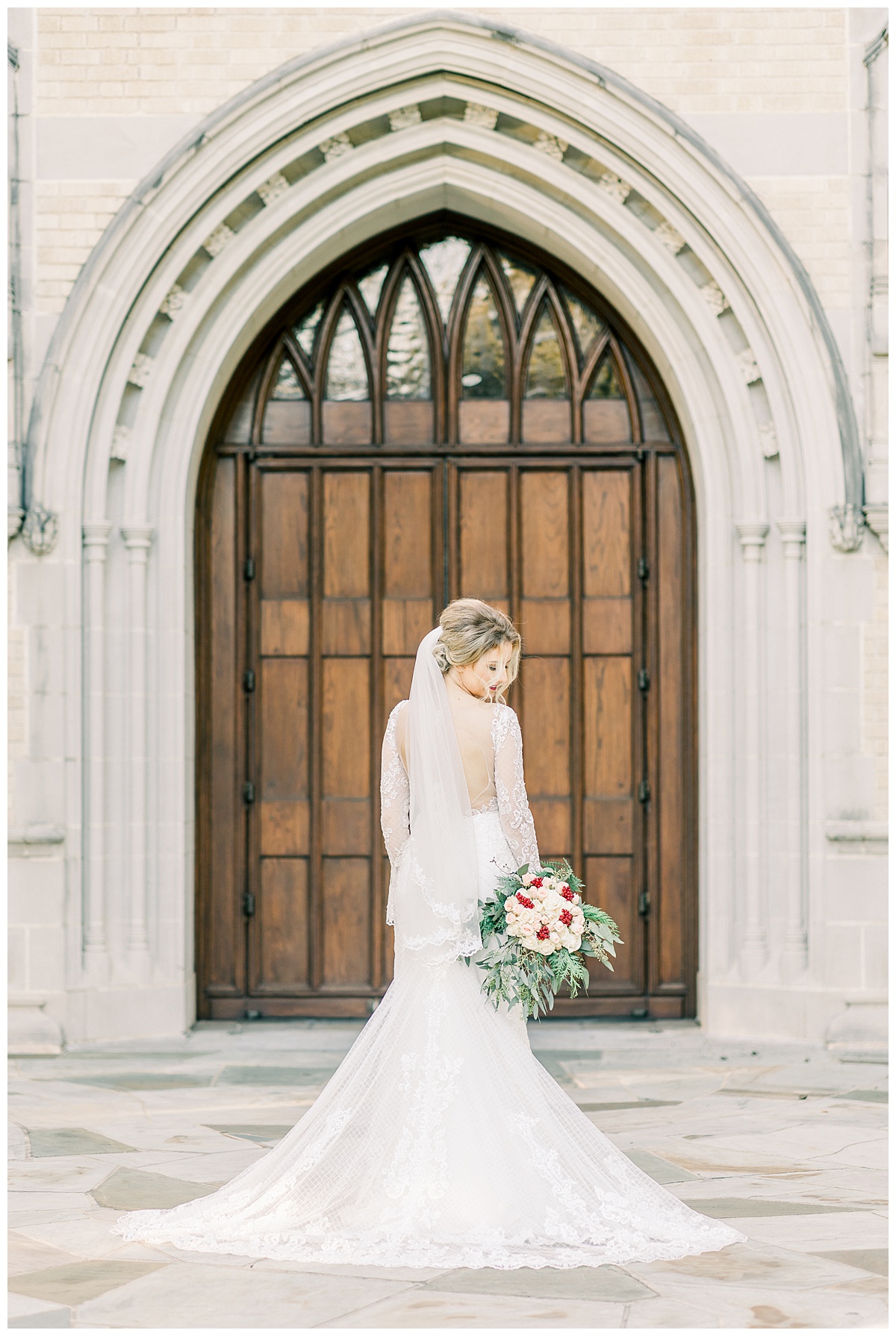Bride in wedding dress standing in front of wooded church doors looking down at bouquet